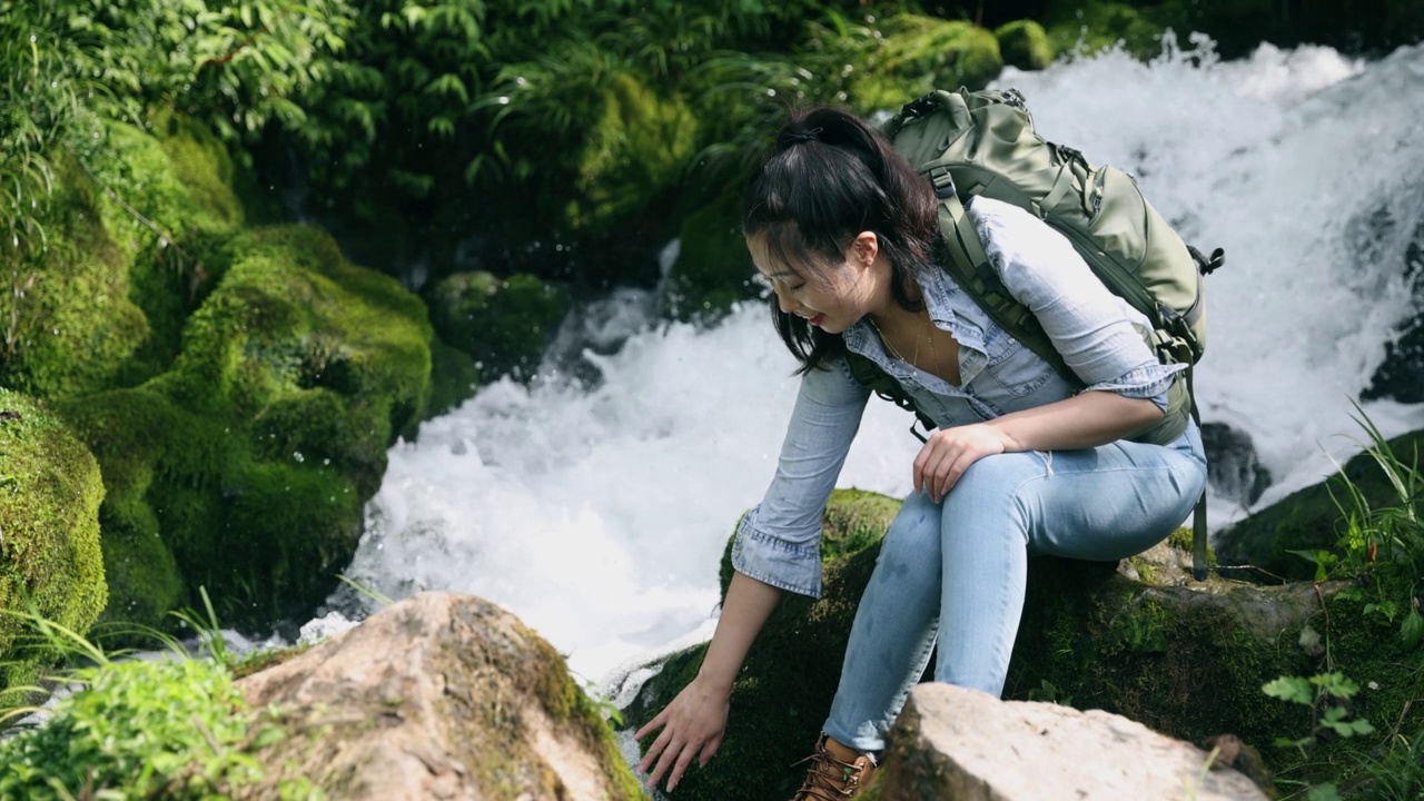 女徒步旅行者坐在瀑布旁休息视频素材