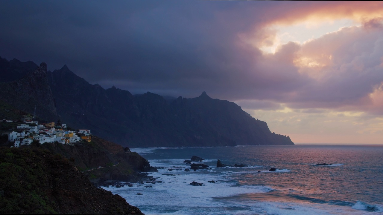 大西洋日落，Roques de Anaga。巨大的波浪形成泡沫和巨大的火山形成在背景中。黄昏中的小村庄Almaciga。特纳利夫岛北部。加那利群岛。视频素材