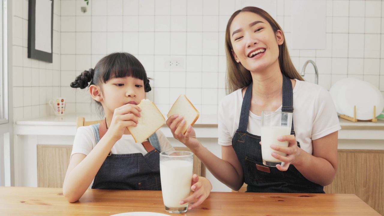 亚洲家庭在客厅享用早餐。小女孩女儿坐在桌子上，和微笑的爸爸妈妈在早上喝牛奶。家庭幸福。视频素材