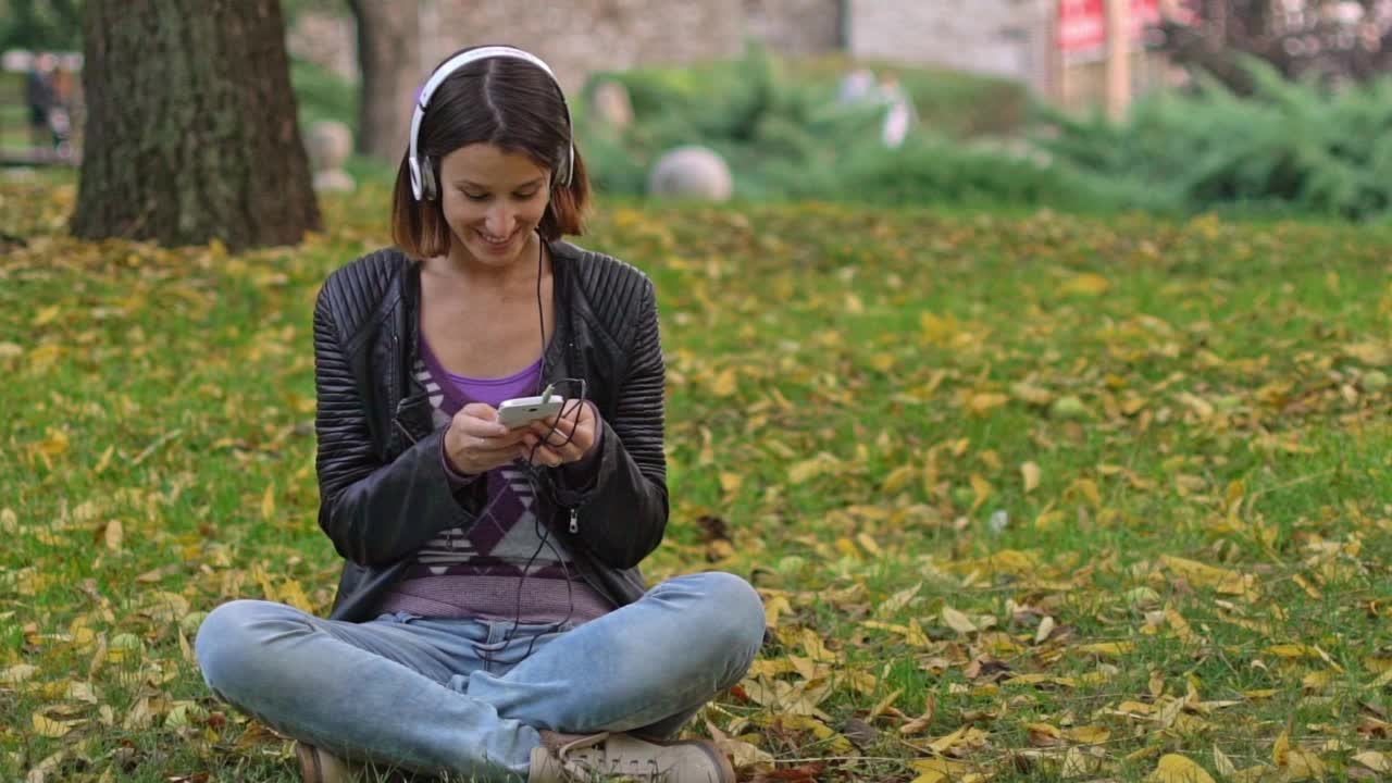 年轻女子在秋天的公园里用智能手机视频素材