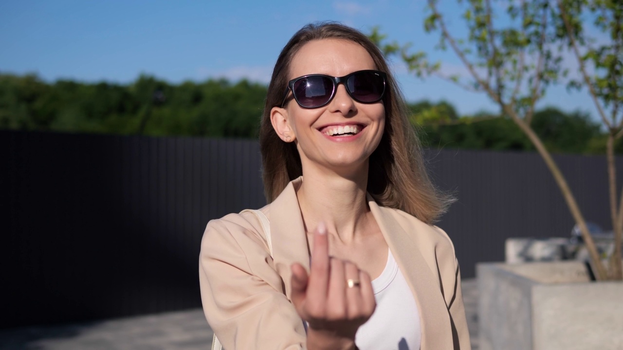 美丽的金发女商人戴着眼镜诱惑友好的女孩调情的女士指着相机微笑做邀请的手势，要求来欢迎的符号作出选择选择。视频素材