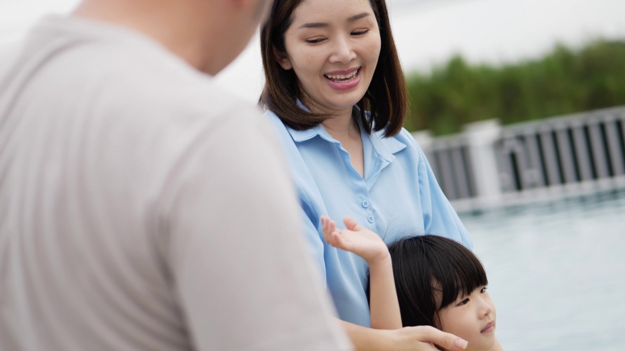 爸爸和妈妈带着两个小男孩在度假村的游泳池里挥手指着什么。视频素材