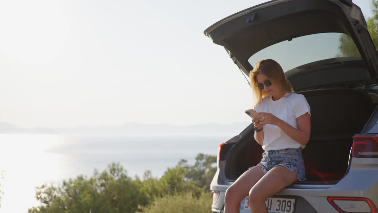 女子在享受夏日海滨公路旅行时使用手机。视频素材