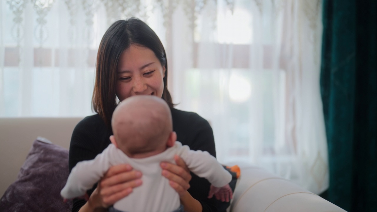 妈妈抱着她的小宝贝在家里的客厅里开心地玩耍、欢笑视频素材