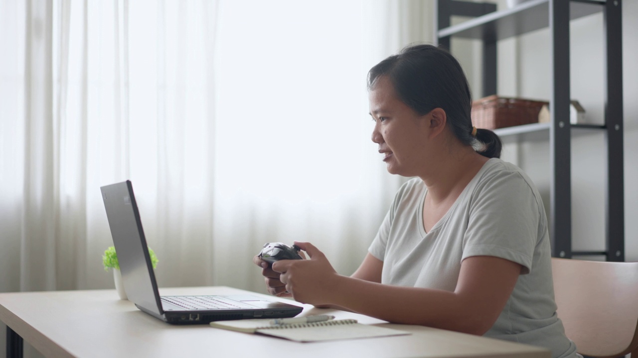 开朗的女人喜欢用他笔记本电脑上的操纵杆玩电子游戏视频素材