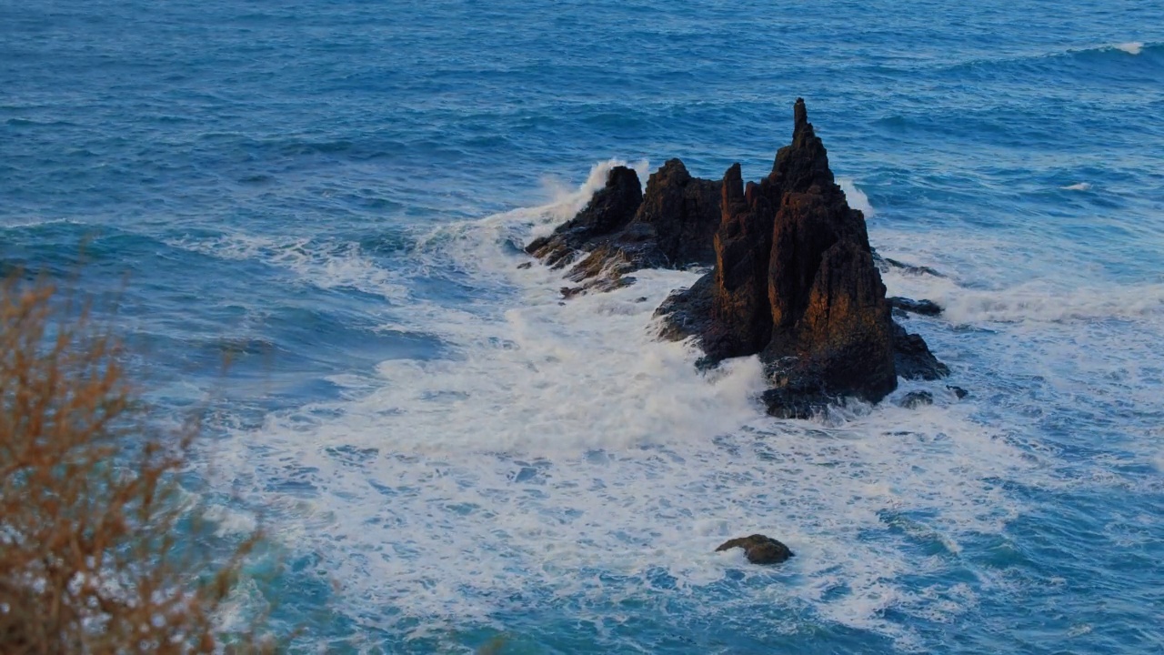 阳光明媚的日子，海浪拍打着岩石火山海岸，形成空气泡沫。特内里费岛的贝尼霍海滩。西班牙加纳利群岛视频素材