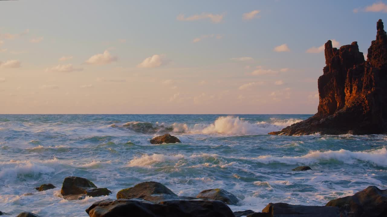 明亮的海上日落。海浪撞击岩石，被温暖的夕阳，鹅卵石，火山玄武岩照亮在特内里费岛。海浪飞溅成白色的泡沫。永恒的自然之美。视频素材