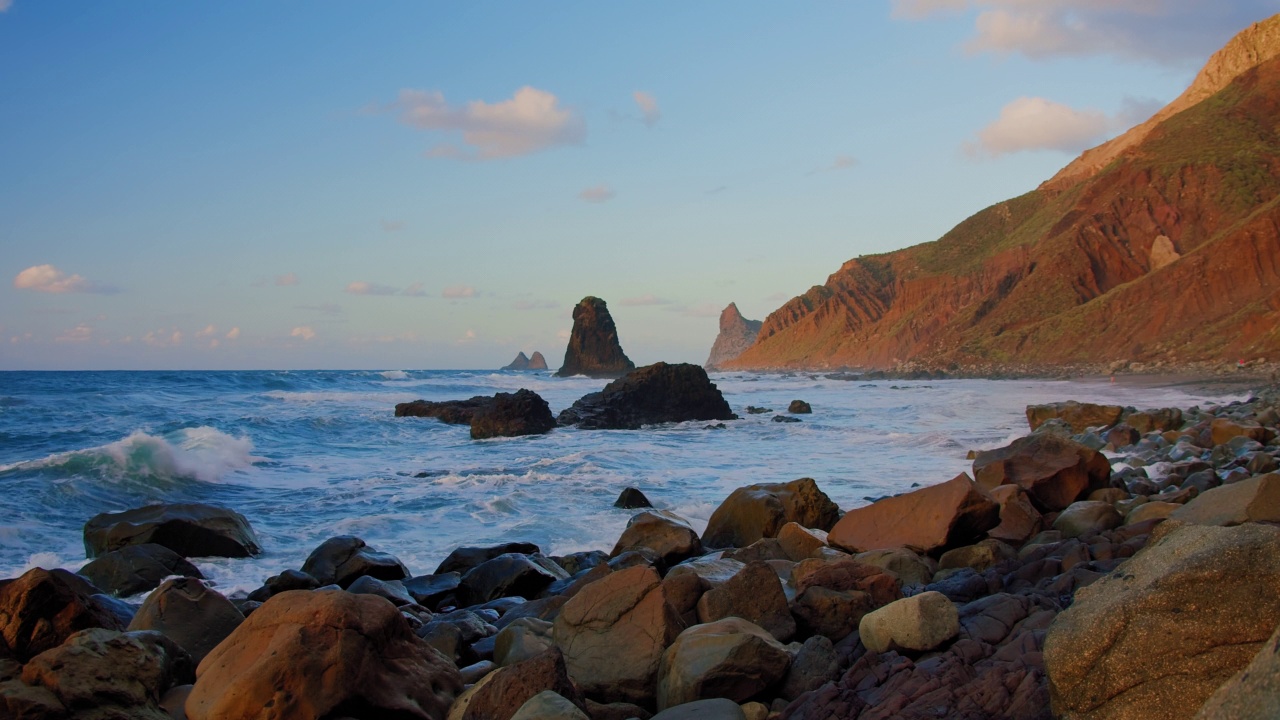 明亮的海上日落。海浪撞击岩石，被温暖的夕阳，鹅卵石，火山玄武岩照亮在特内里费岛。海浪飞溅成白色的泡沫。永恒的自然之美。视频素材