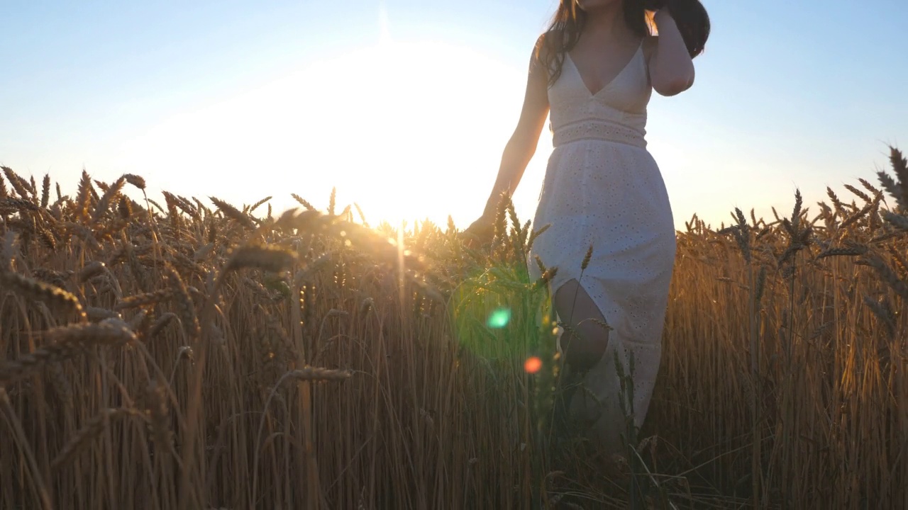 难以辨认的女人站在金色的麦田和举起手在夕阳的背景。年轻的女孩穿着白色的衣服享受自由或风景优美的夏天。与自然和谐。慢动作视频素材