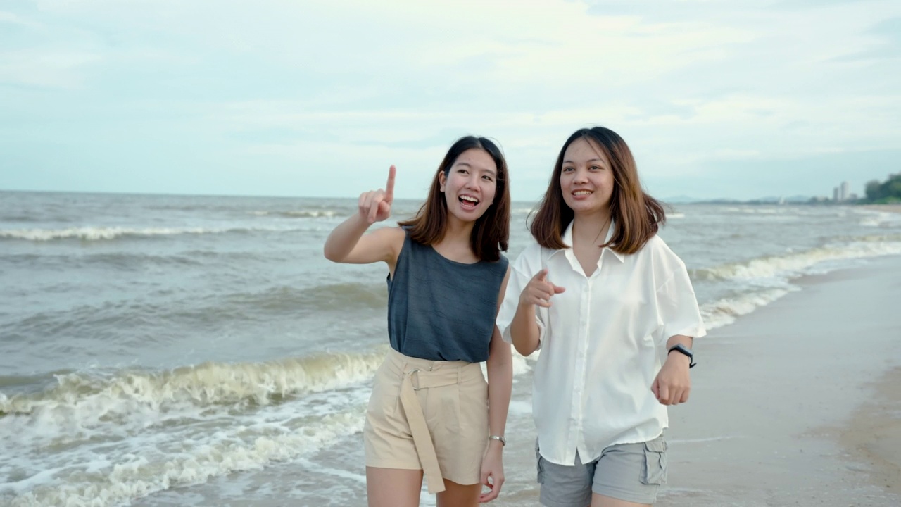 两个亚洲女人是最好的朋友，周末旅行，在一个晴朗的日子，日落前沿着海滩散步，愉快地聊天。海滨地区是一个旅游胜地视频素材