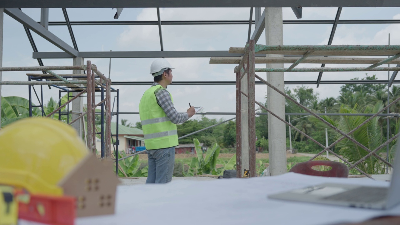 在建筑工地，身穿橙色反光背心的工程师或检查人员正在用写字板做笔记和检查。视频素材