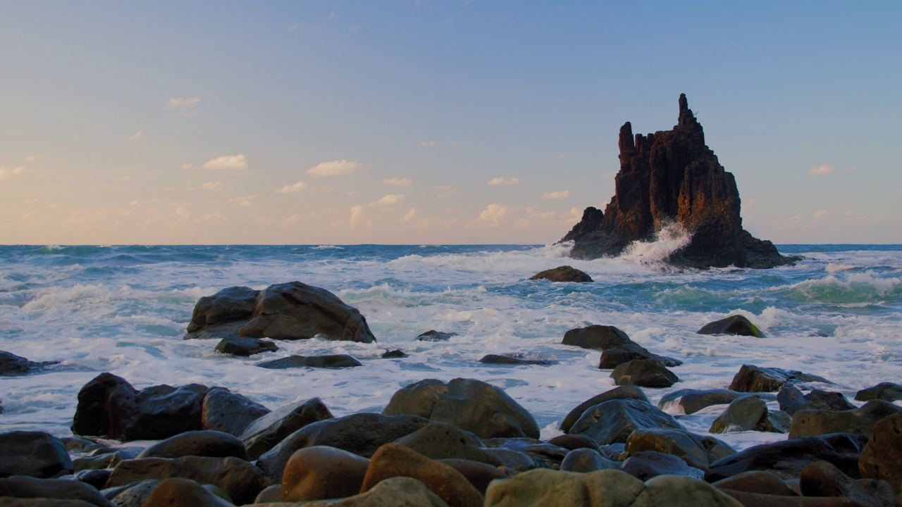 明亮的海上日落。海浪撞击岩石，被温暖的夕阳，鹅卵石，火山玄武岩照亮在特内里费岛。海浪飞溅成白色的泡沫。永恒的自然之美。视频素材