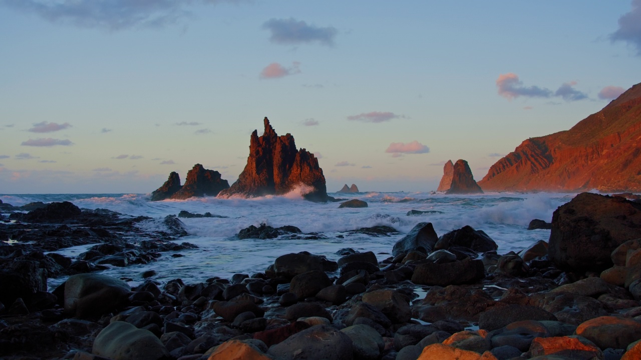 明亮的海上日落。海浪撞击岩石，被温暖的夕阳，鹅卵石，火山玄武岩照亮在特内里费岛。海浪飞溅成白色的泡沫。永恒的自然之美。视频素材