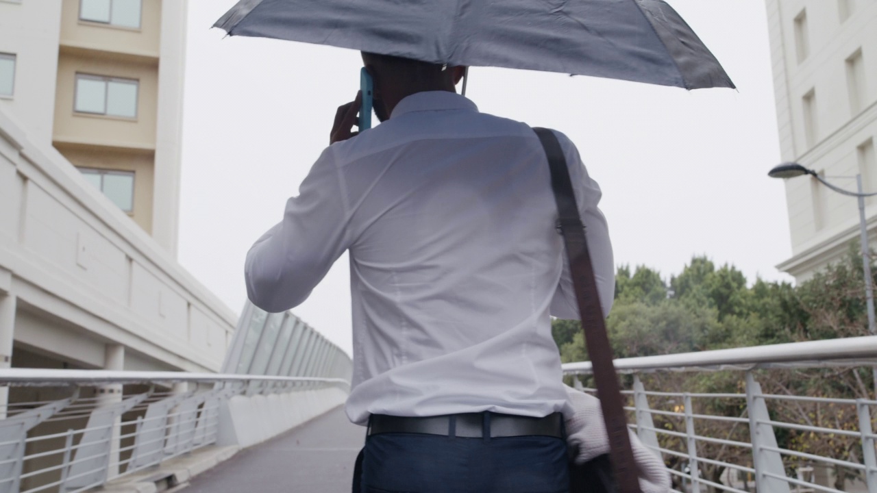 回顾年轻的商人在雨中打着伞走在城市里打电话的情景。在冬天通勤上班。提供保险的拉丁公司保险代理人视频素材