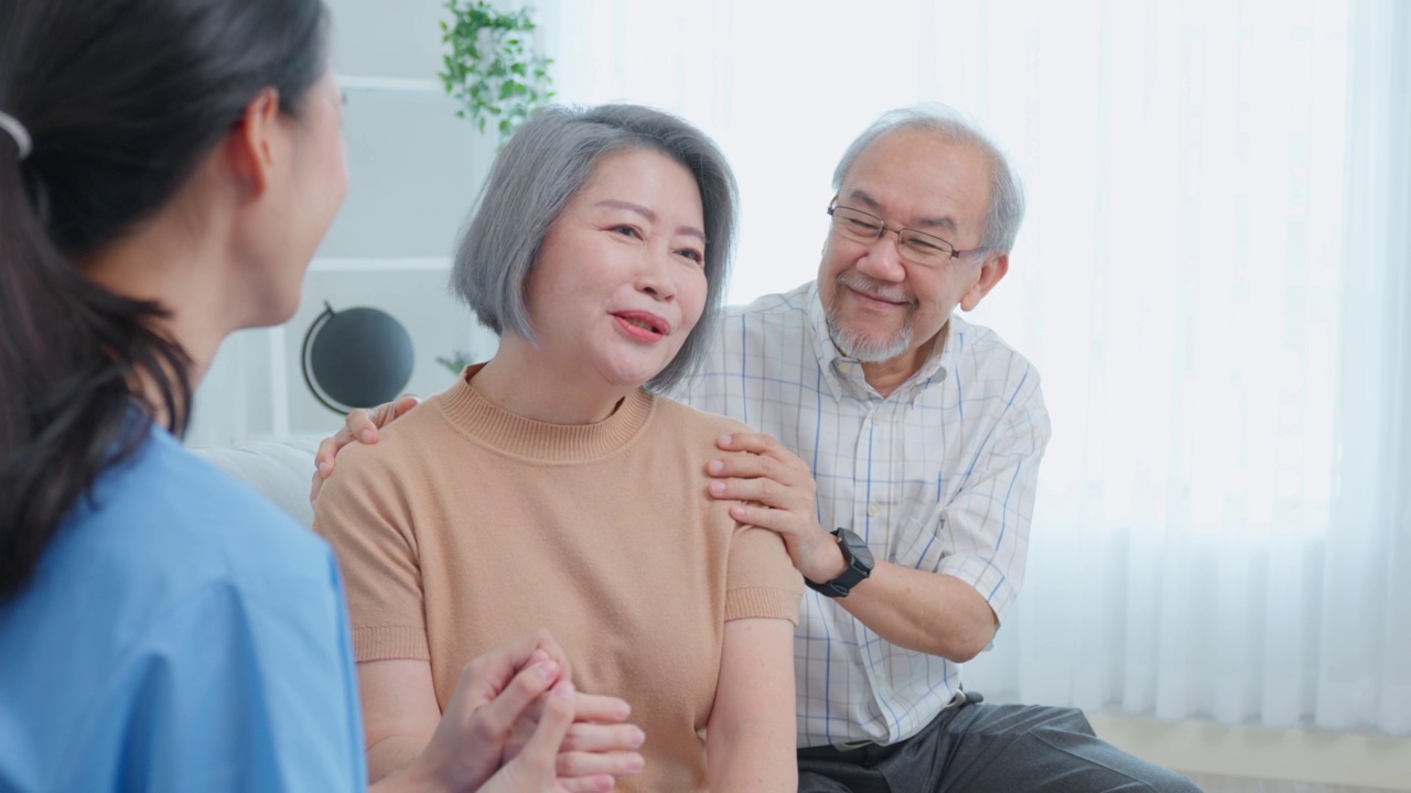 亚洲护理护士在家检查老年妇女病人和丈夫。有吸引力的年轻专家护理妇女支持给予建议和咨询年长的成熟夫妇在客厅的房子视频素材