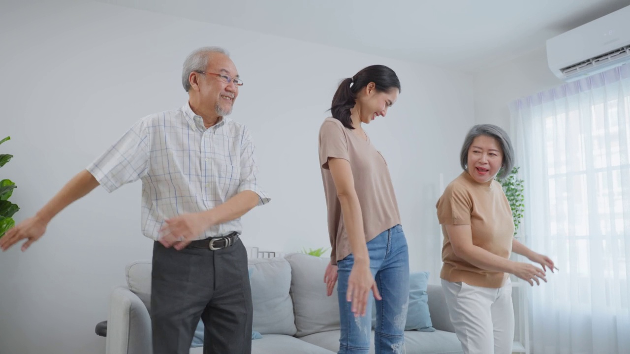 亚洲有趣的高级夫妇和女儿一起在客厅跳舞。有吸引力的漂亮女人和年长成熟的祖父母感觉愉快的度过休闲时间，在周末听音乐在家里。视频素材