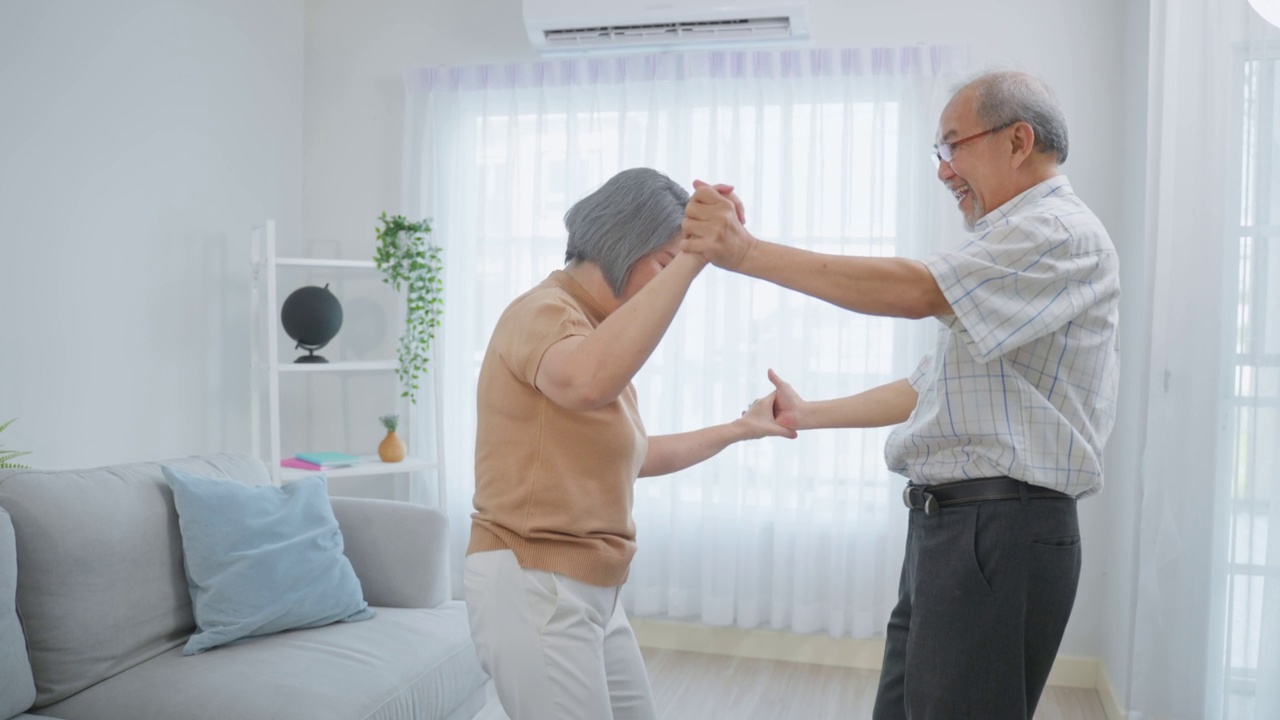 亚洲活跃的老年夫妇喜欢在家里的客厅一起跳舞。年老的祖父和祖母微笑着感觉相爱，享受关系和退休后的房子里的活动。视频素材