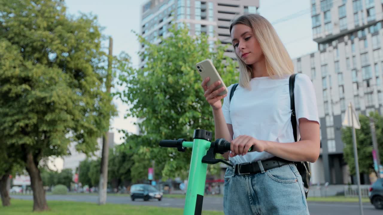 在城市里，一名美女骑上电动车后正在使用智能手机。一名女子在电动滑板车附近用智能手机发短信。视频素材