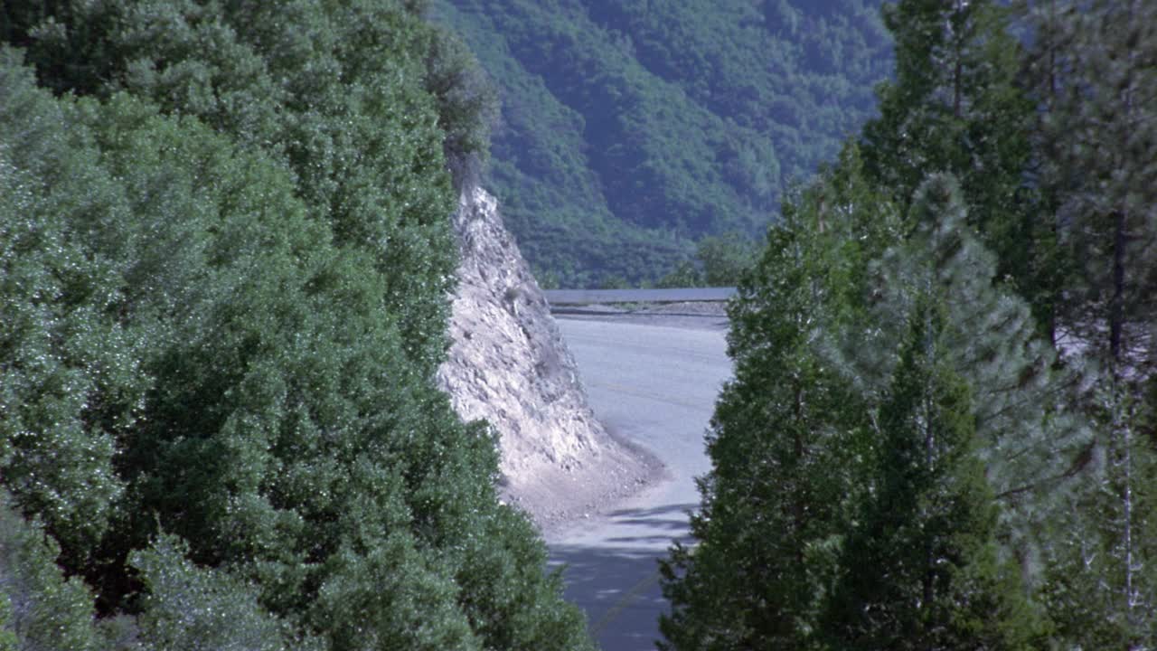 长满常青树的山腰。看到蜿蜒的道路沿着山的一侧运行。看到棕褐色的凯迪拉克在路上行驶视频素材