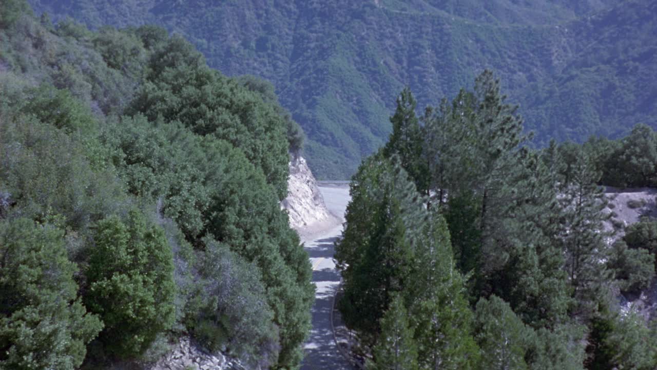 褐色和棕色的凯迪拉克沿着山边的道路行驶的航拍。看见路边有树视频素材