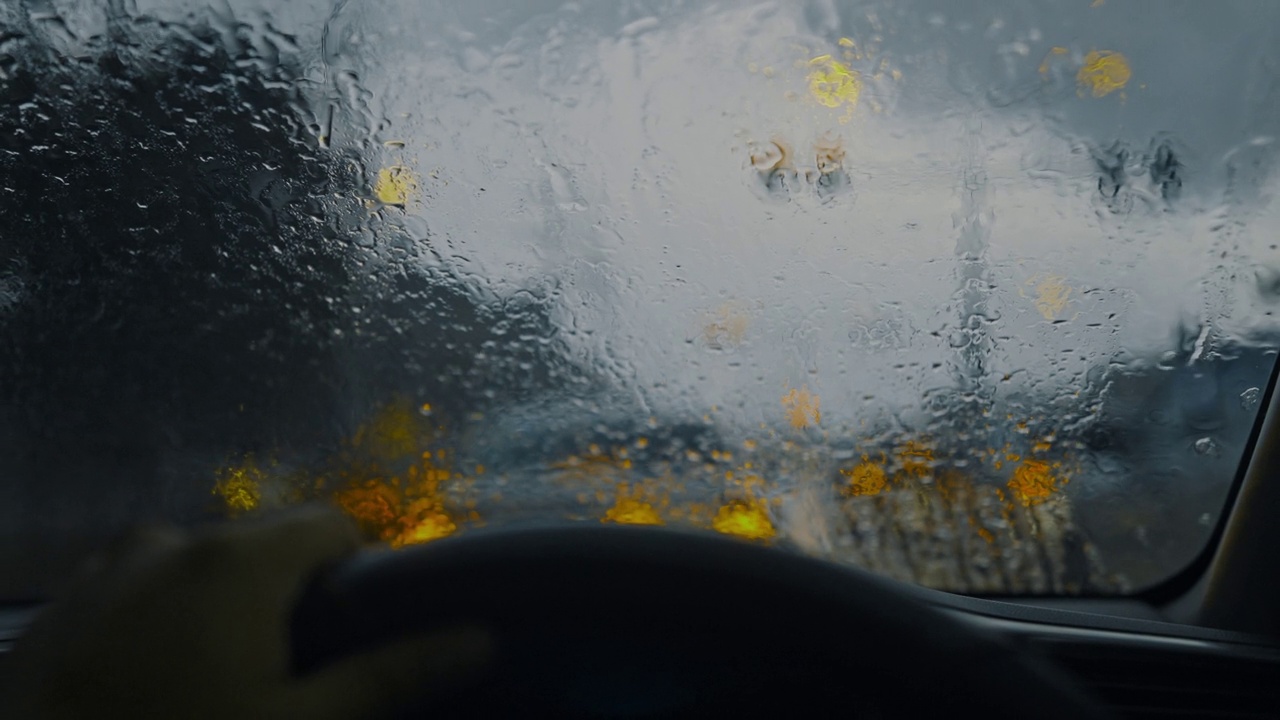 从生态车内部观察年轻的成年女性手驾驶方向盘汽车在雨季的道路上视频素材