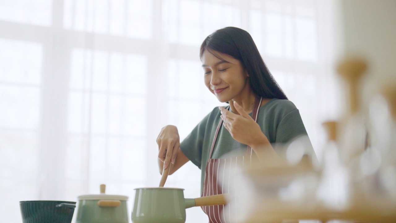 年轻美丽的亚洲女人在家里厨房做饭视频素材