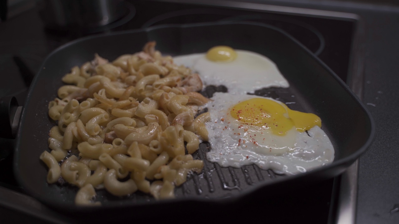 在平底锅中准备炒鸡蛋和面条，撒上调味料、香料和盐。用手给食物调味。烹饪过程的概念。香料。热盘子里的炒鸡蛋视频素材