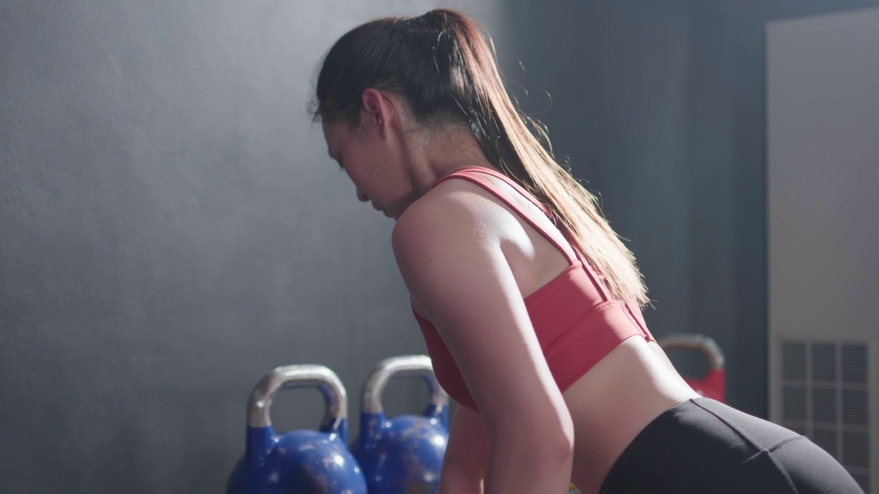 年轻的亚洲女性做训练举重壶铃侧面视图在健身房里锻炼。健身运动员漂亮的女孩穿着运动服持有壶铃。健康的生活方式的概念。视频素材