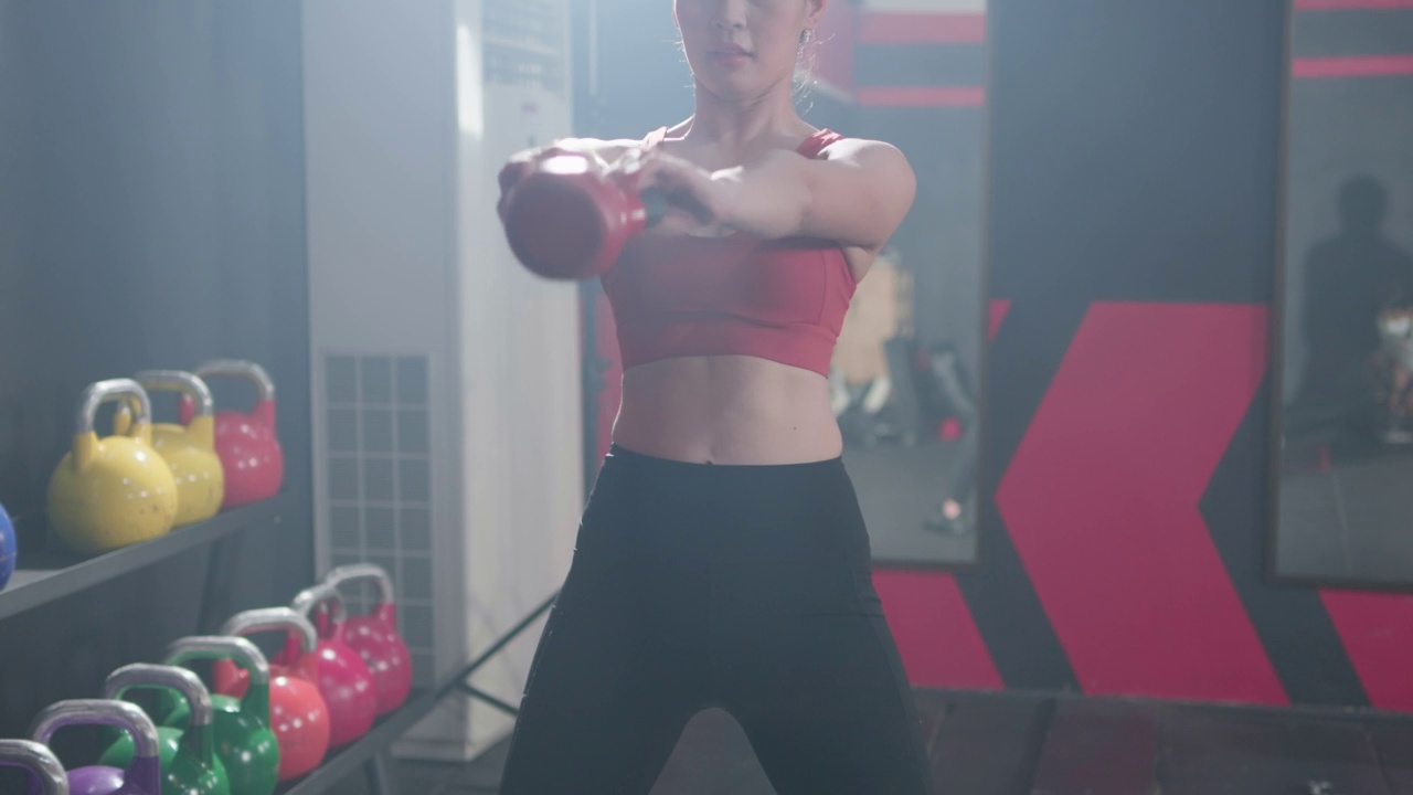 迷人的亚洲年轻女性做训练举重壶铃在健身房里锻炼。健身运动员漂亮的女孩穿着运动服持有壶铃。视频素材