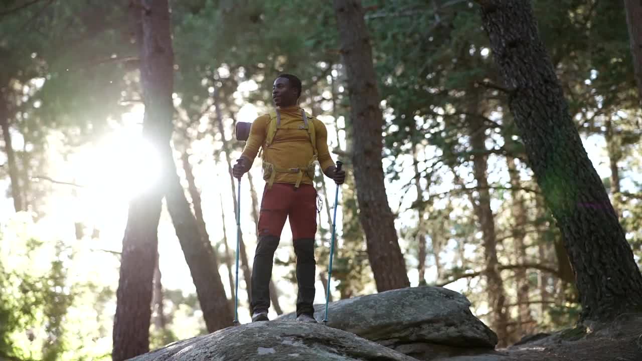 一个非裔美国人在日落时站在岩石上。背着背包和扁担在山上徒步或越野视频素材