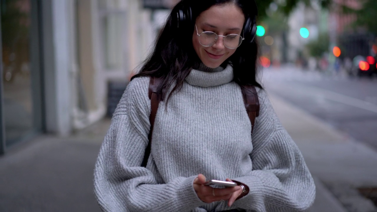 快乐的女人在蓝牙耳机听积极的音乐播放列表和舞蹈在城市设置视频素材