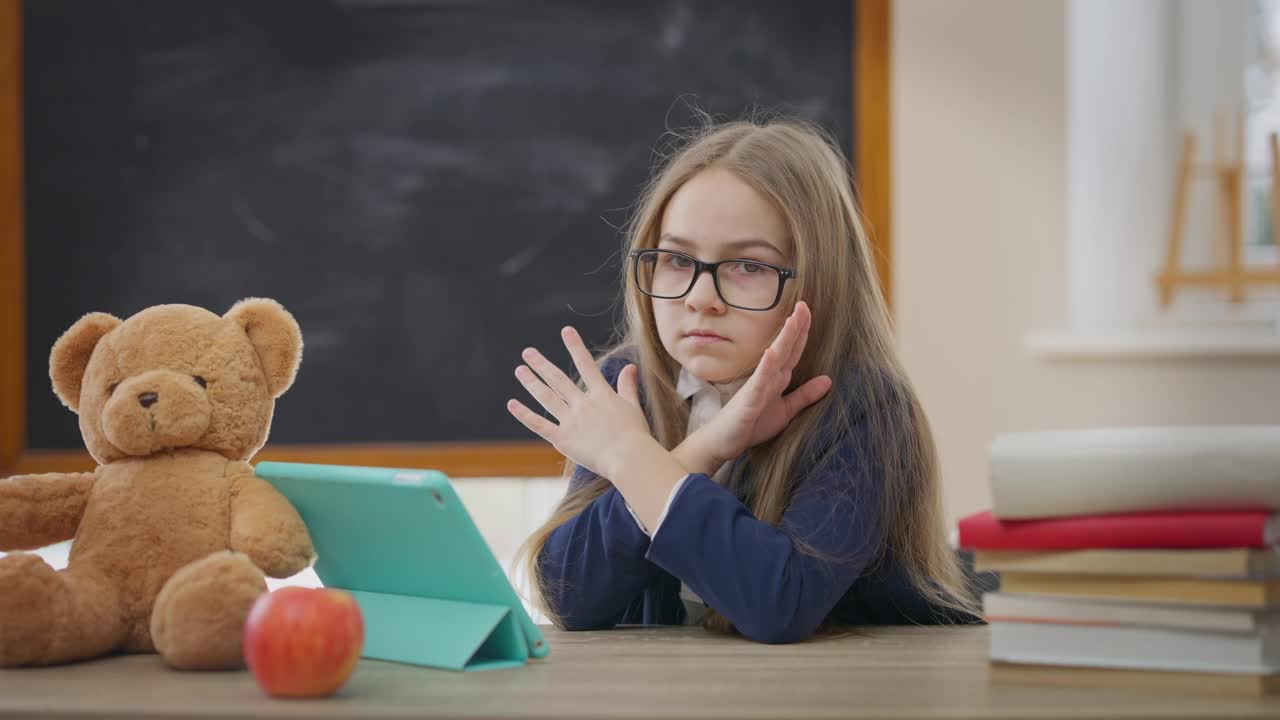 精疲力竭的白人女孩手势没有交叉看着镜头坐在学校教室的书桌。疲惫的女学生在室内摆姿势的肖像。回到学校概念。视频素材