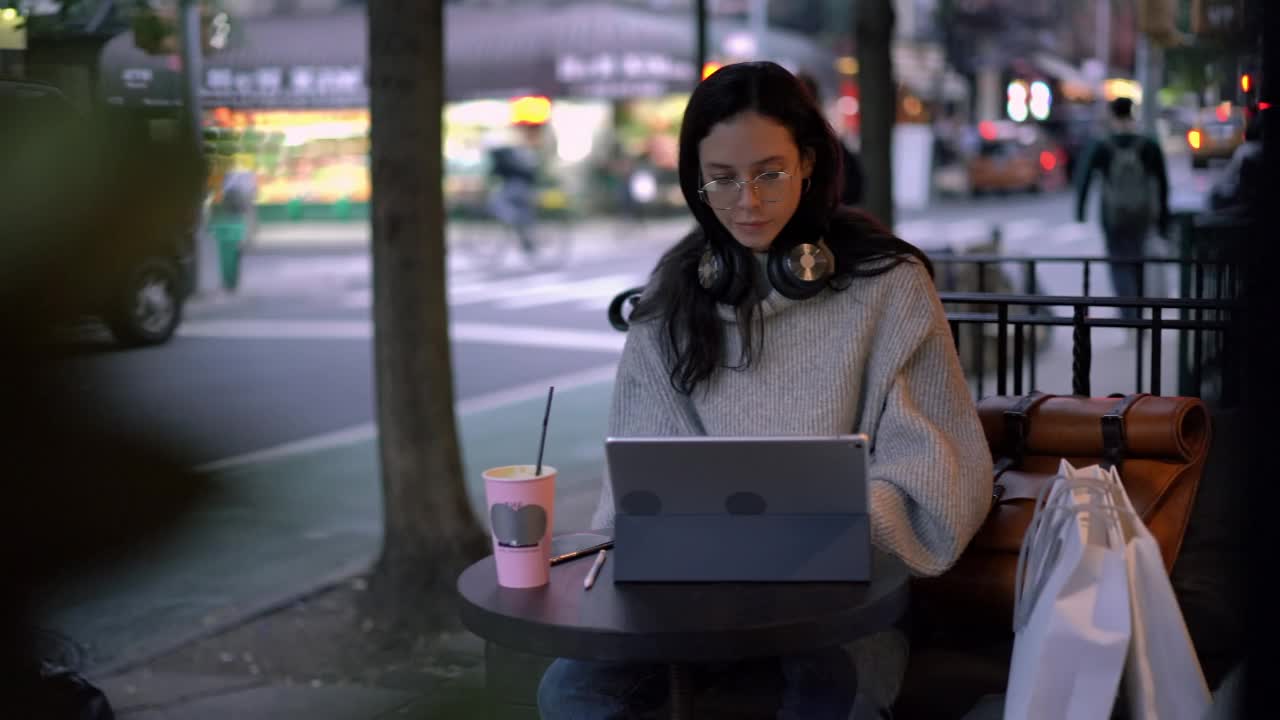 美丽的白人女性戴着眼镜，在人行道上的自助餐厅使用现代设备视频素材