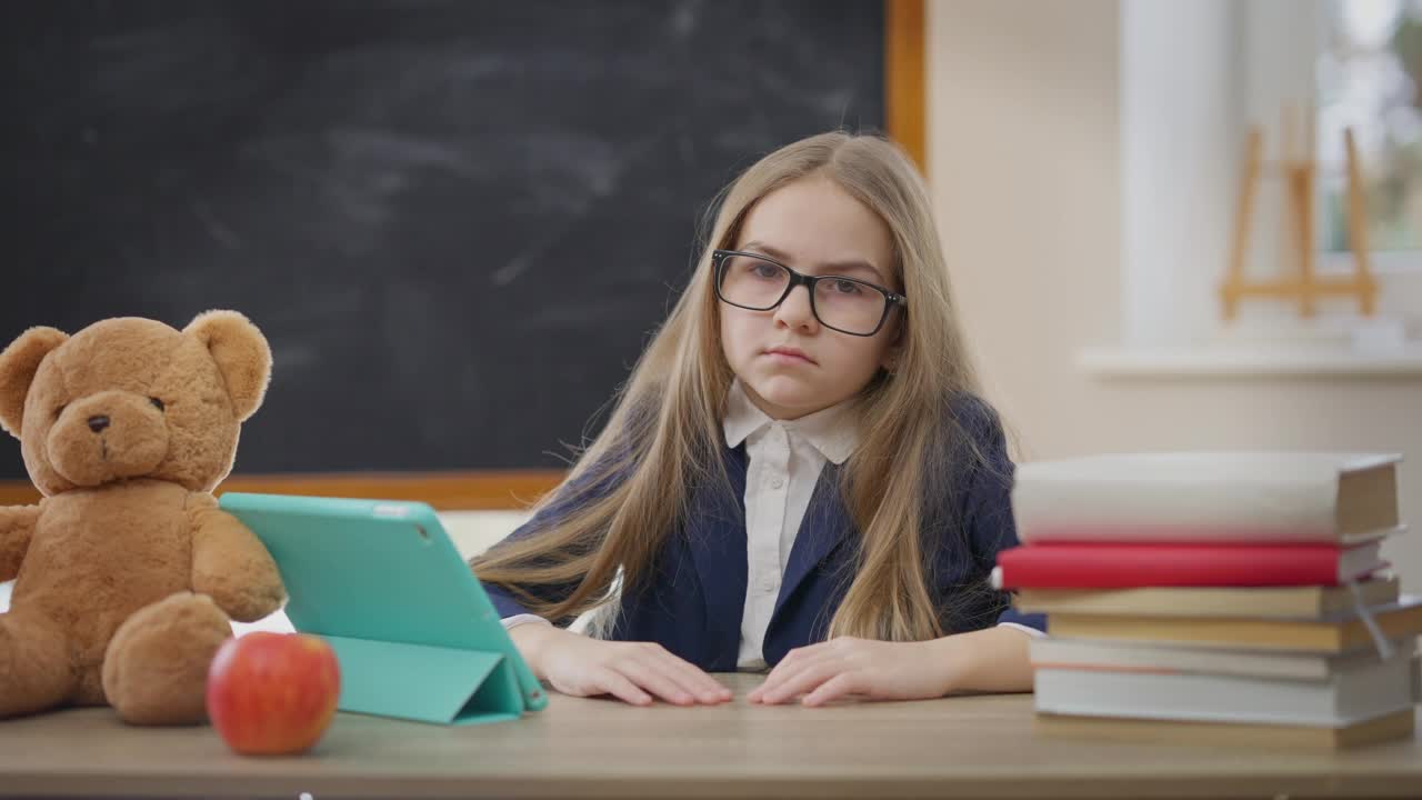 不满的白人女学生用手指向下看着镜头，脸上带着疲惫的表情。在学校室内，疲惫不堪的学生在教室里摆姿势。视频素材