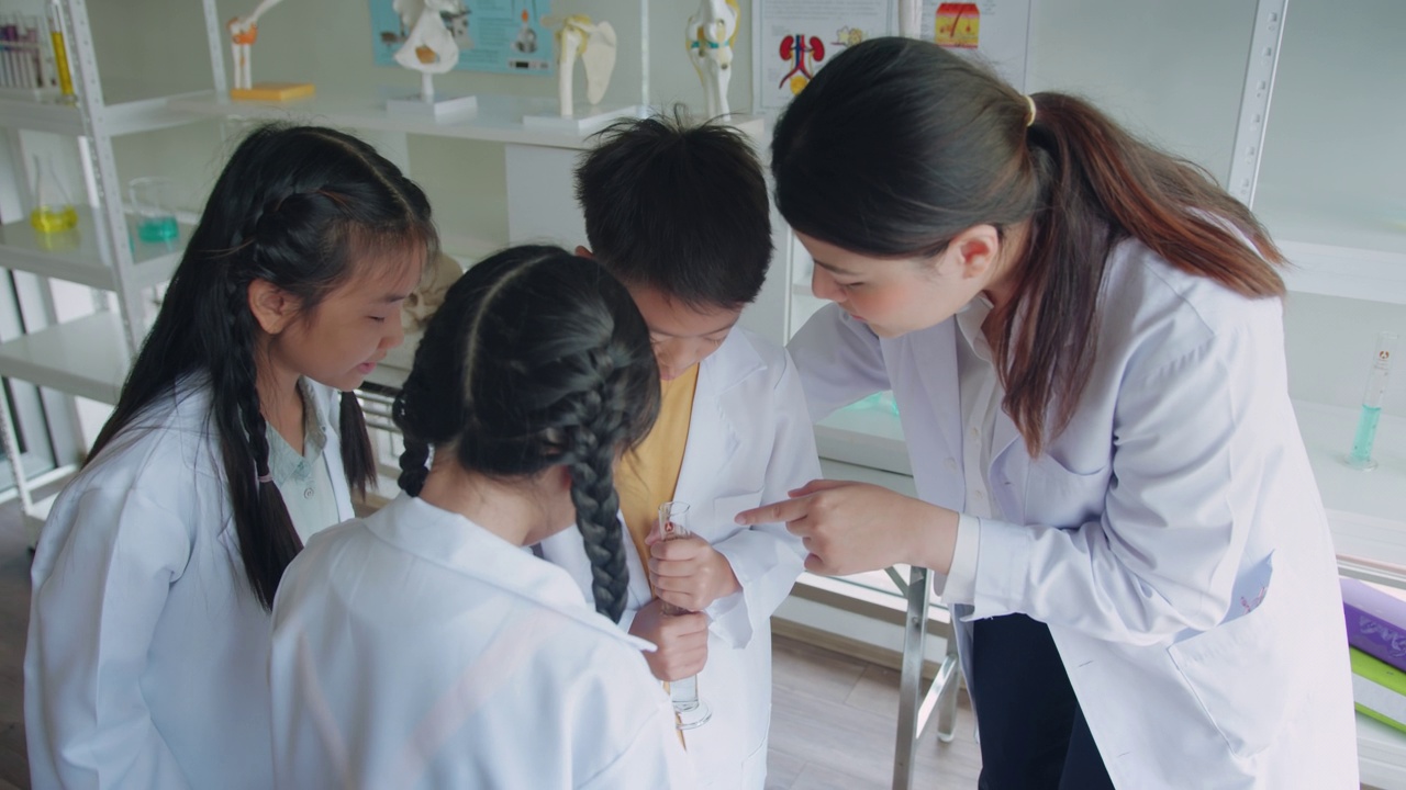 教师授课并向小学生讲解化学。他们在学校实验室的烧杯中学习科学和化学混合。视频素材