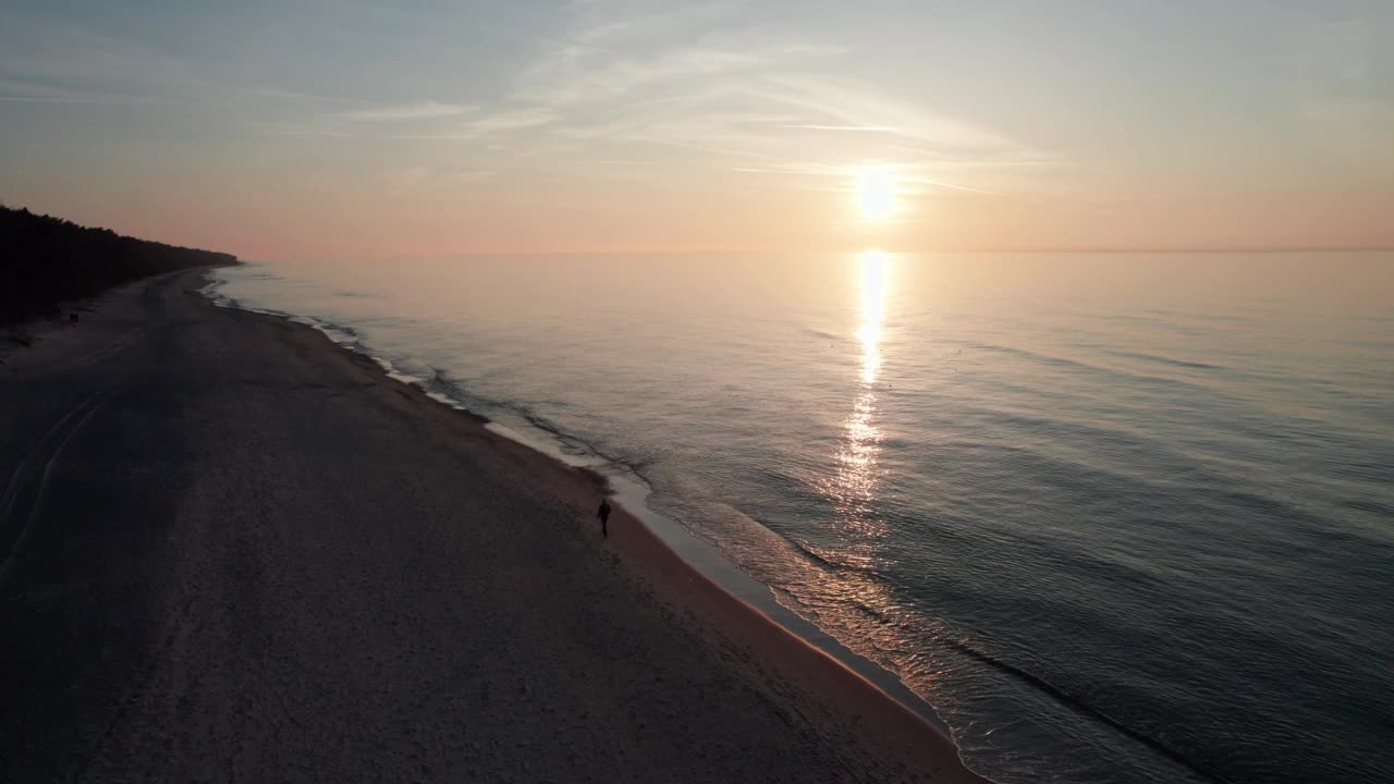 夕阳下空旷的海滩，无人机在水面上飞行，反射出天空的橙色。视频素材