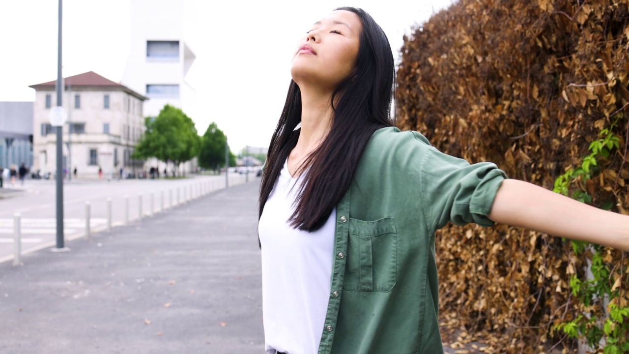 女人站在城市里，闭着眼睛，张开双臂视频素材