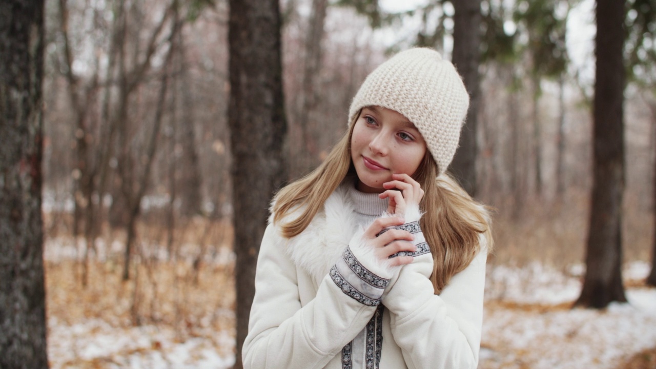 年轻的金发白衣漂亮女孩在冬季雪林下午摆拍侧视神秘微笑。中景镜头视频素材