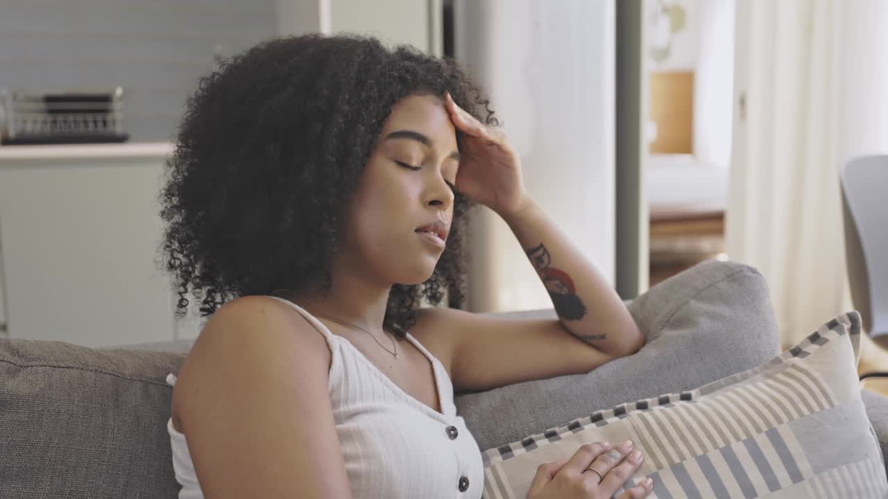 压力大的年轻女性坐在家里的沙发上头痛。一个生病的或不快乐的女性，伴有疼痛的偏头痛，感觉身体和精神上的枯竭和疲劳视频素材