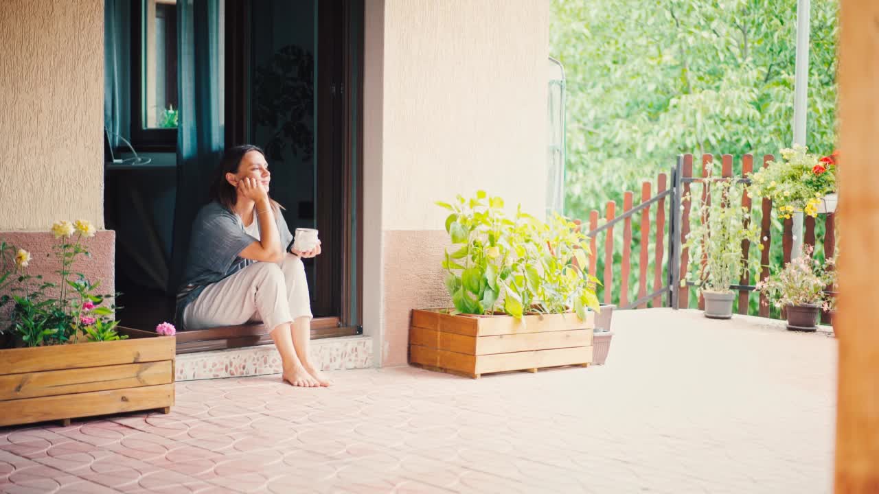 一位年轻的成年女性坐在露台上享受她的早茶视频素材