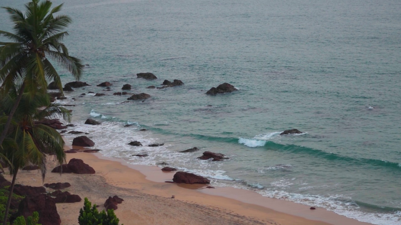 在印度果阿的Cabo De Rama海滩海滩旁的棕榈树。海浪拍打着海滩的海岸。夏季热带海滩背景。果阿邦海滩干净，没有游客。视频素材