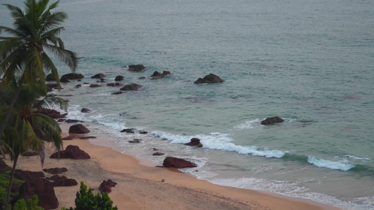 在印度果阿的Cabo De Rama海滩海滩旁的棕榈树。海浪拍打着海滩的海岸。夏季热带海滩背景。果阿邦海滩干净，没有游客。视频素材