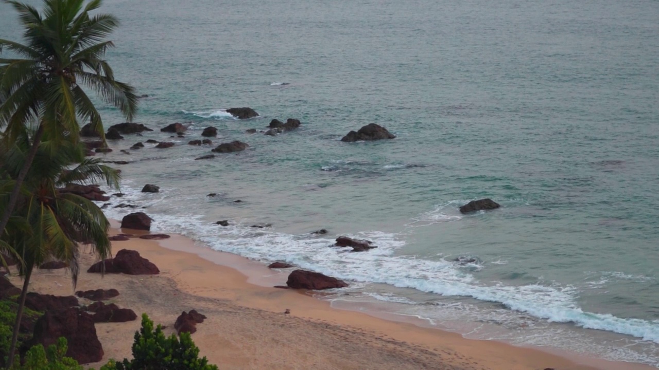 在印度果阿的Cabo De Rama海滩海滩旁的棕榈树。海浪拍打着海滩的海岸。夏季热带海滩背景。果阿邦海滩干净，没有游客。视频素材