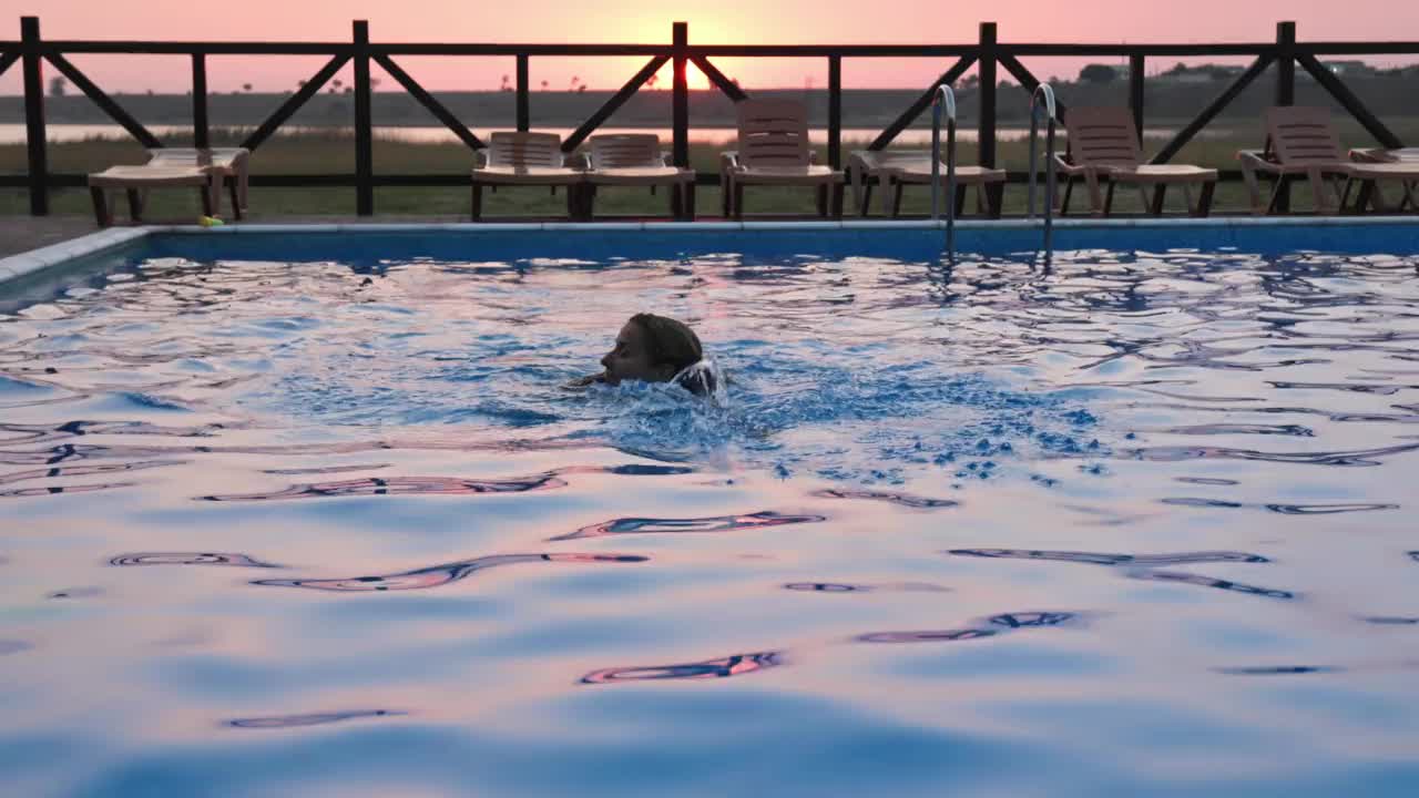 一个女人游泳在一个清澈的水的背景是一个夏天的夕阳度假视频素材