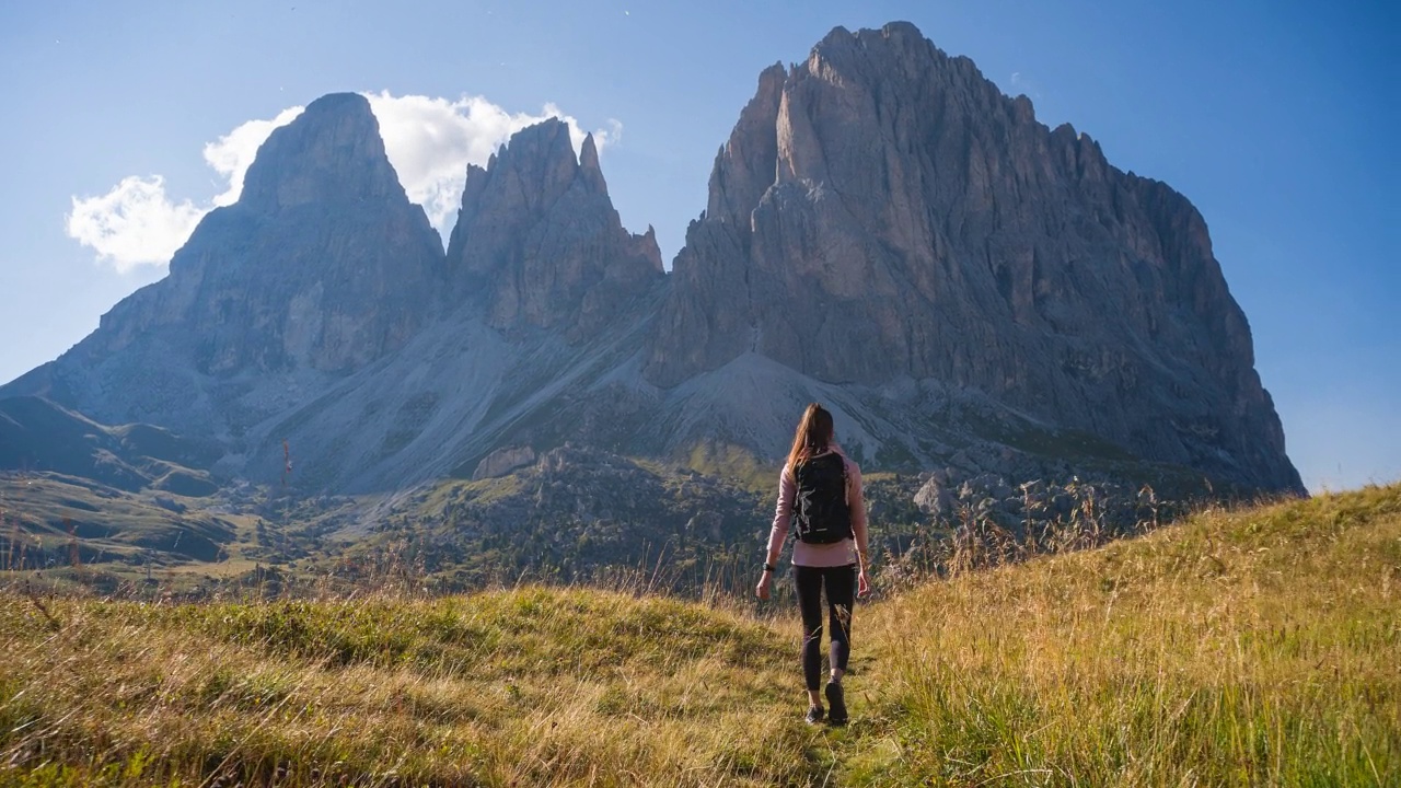 女人是活跃的，在雄伟的山前面的草地上徒步旅行视频素材