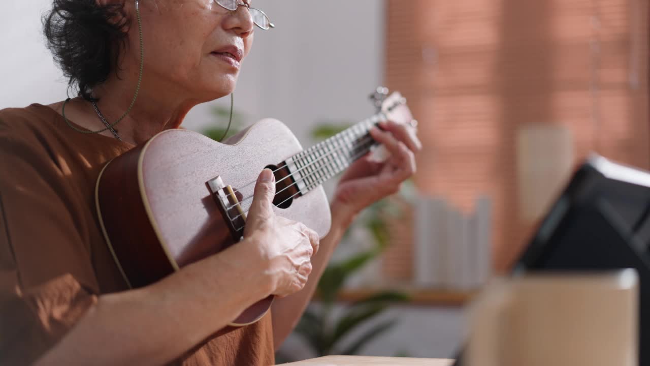 退休的老年妇女坐在客厅用笔记本电脑在家在线学习吉他视频素材