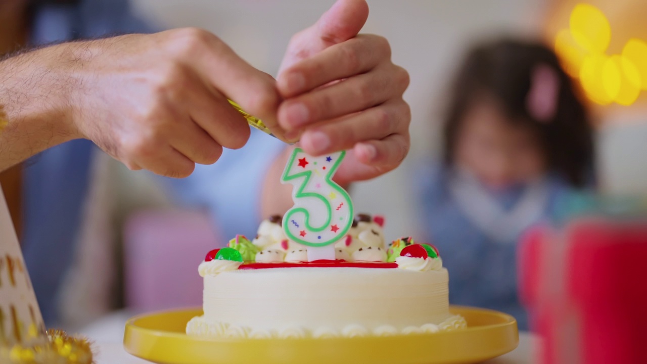 女儿三岁生日聚会在家里庆祝，全家人帮她吹灭客厅里的蜡烛，气球和五颜六色的装饰物品到处都是，女孩是大笑微笑的喜悦视频素材