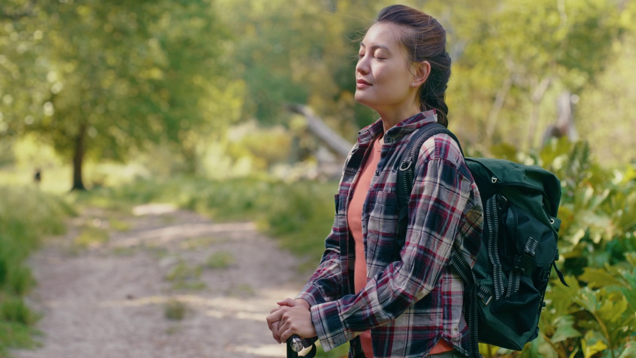 在森林小径远足时呼吸新鲜空气的女性。适合背包客在偏远的环境中探索自然和美丽的风景，郁郁葱葱的植物和树木。是时候旅行和冒险了视频素材