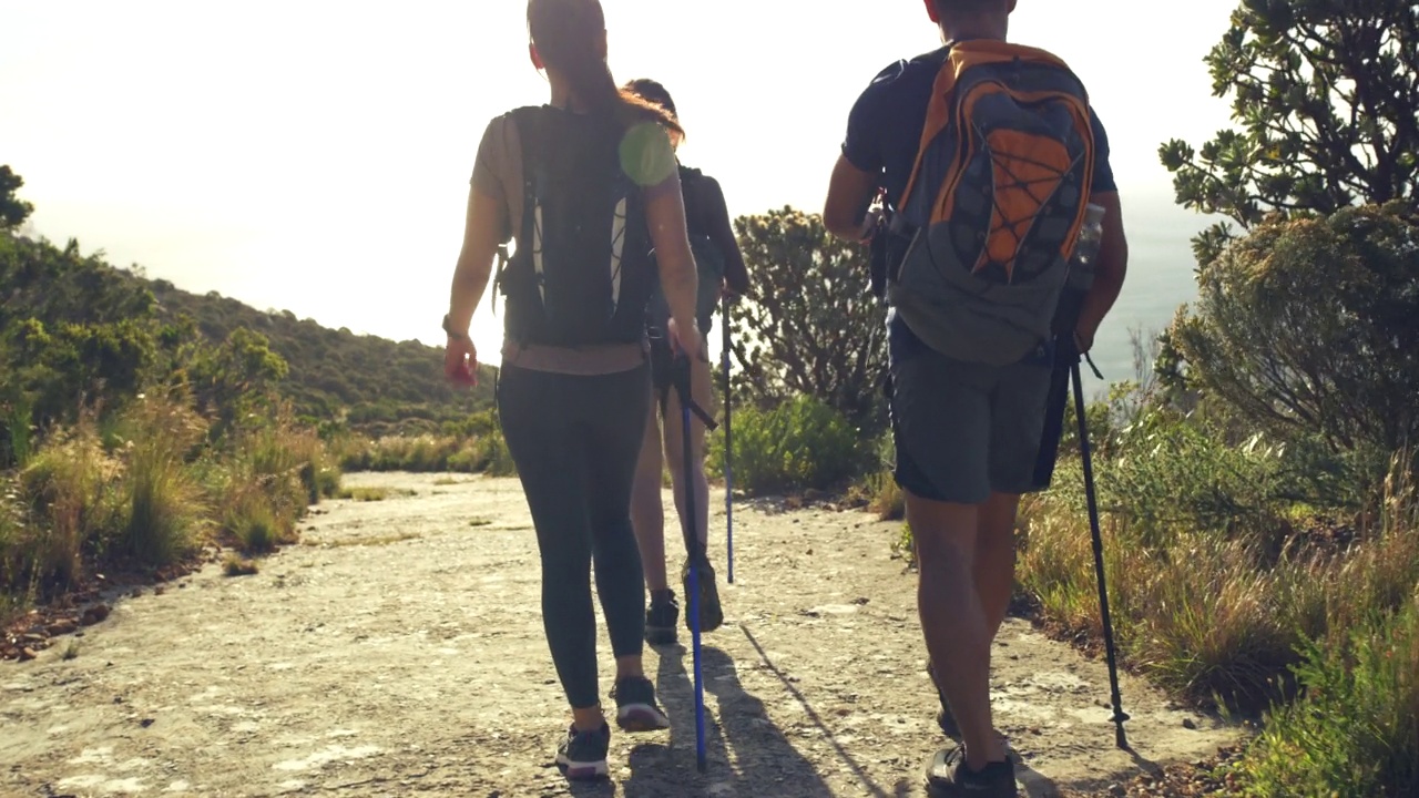 三个朋友拿着杆子在户外的山路上徒步旅行。年轻的徒步旅行者在大自然中散步，欣赏风景，享受积极的体育爱好。保持健康和探索视频素材