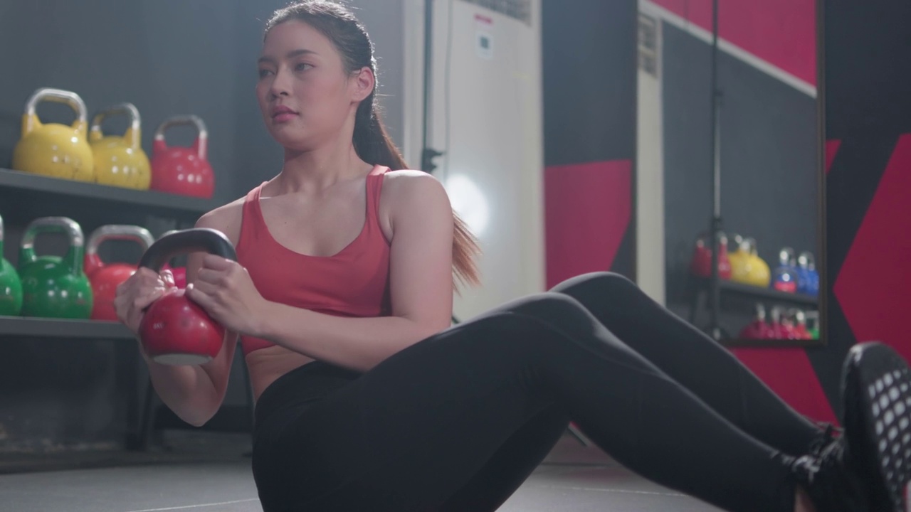 迷人的亚洲年轻女性做训练举重壶铃在健身房里锻炼。健身运动员漂亮的女孩穿着运动服持有壶铃。健康的生活方式的概念。视频素材